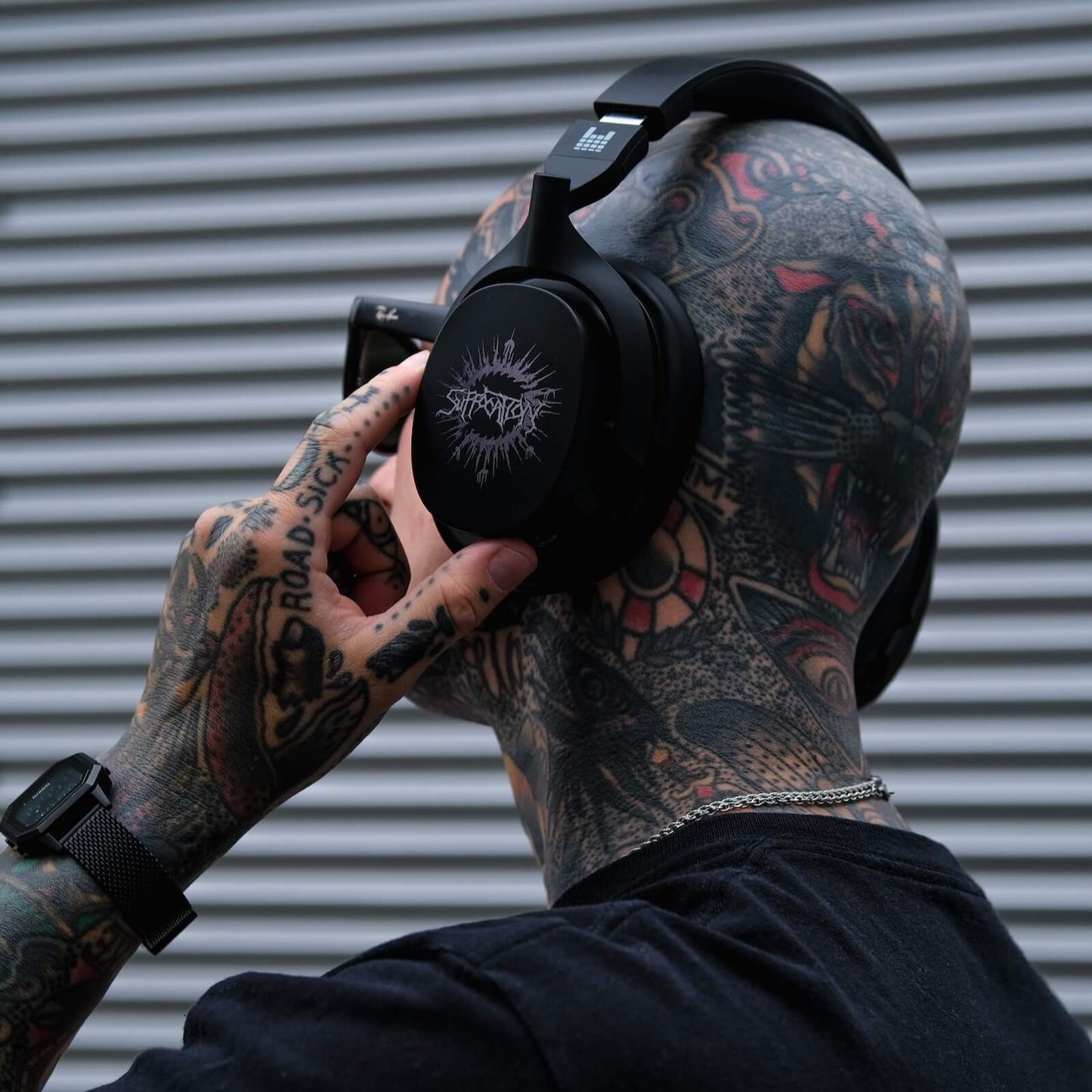 Person with tattoos wearing black heavys headphones against a metallic background