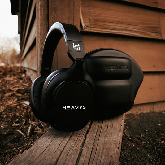 Black Heavys H1H headphones and travel case on a wooden plank beside a wooden wall