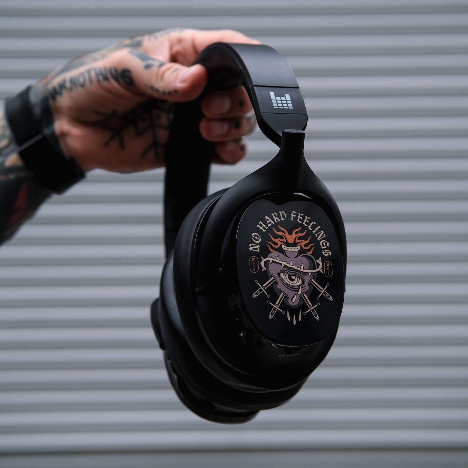 Black headphones heavys h1h  held by a person with tattoos against a gray background